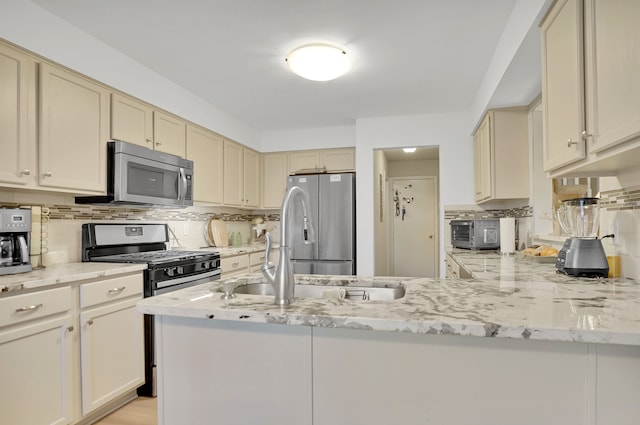 kitchen featuring light stone counters, cream cabinets, stainless steel appliances, a peninsula, and backsplash