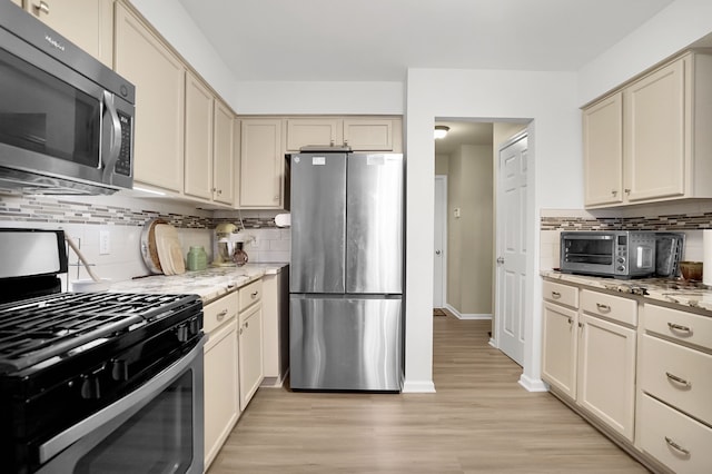 kitchen with light wood finished floors, a toaster, tasteful backsplash, appliances with stainless steel finishes, and light stone counters