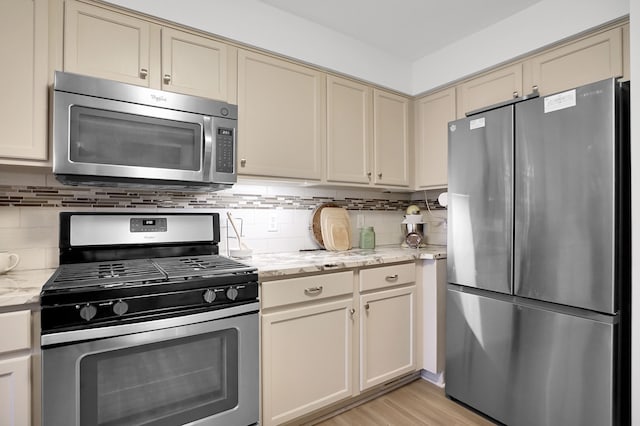 kitchen with light wood finished floors, appliances with stainless steel finishes, backsplash, and cream cabinetry