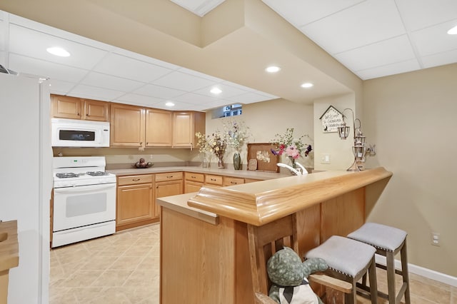 kitchen with white appliances, a drop ceiling, a breakfast bar, a peninsula, and light countertops