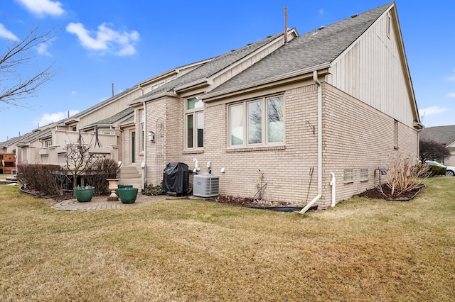 back of property with a shingled roof, cooling unit, a lawn, and brick siding