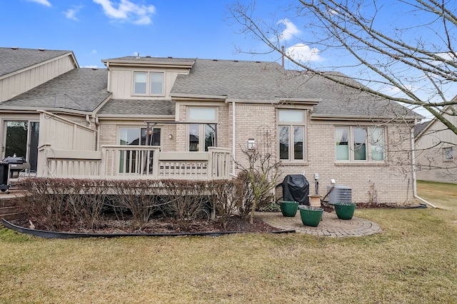 rear view of property featuring a yard, brick siding, a shingled roof, and a wooden deck