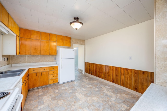 kitchen with light countertops, brown cabinetry, wainscoting, wooden walls, and white appliances