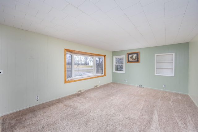 empty room featuring built in shelves, visible vents, carpet floors, and baseboards