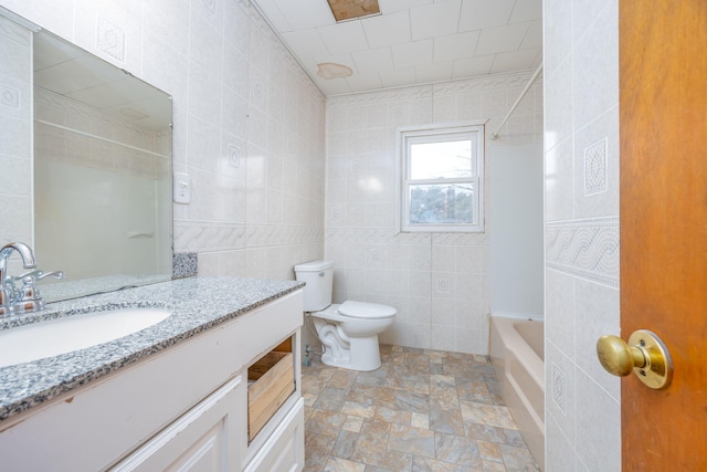 bathroom with toilet, stone finish floor, vanity, and tile walls