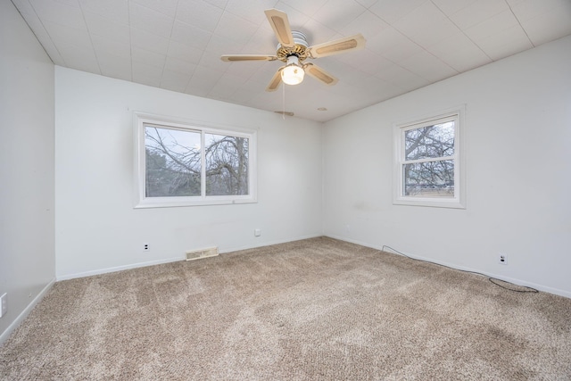 carpeted empty room with a healthy amount of sunlight, ceiling fan, visible vents, and baseboards