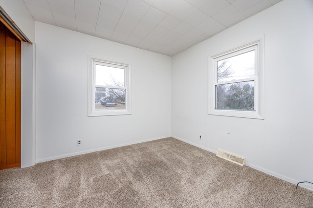 empty room with carpet, visible vents, and baseboards