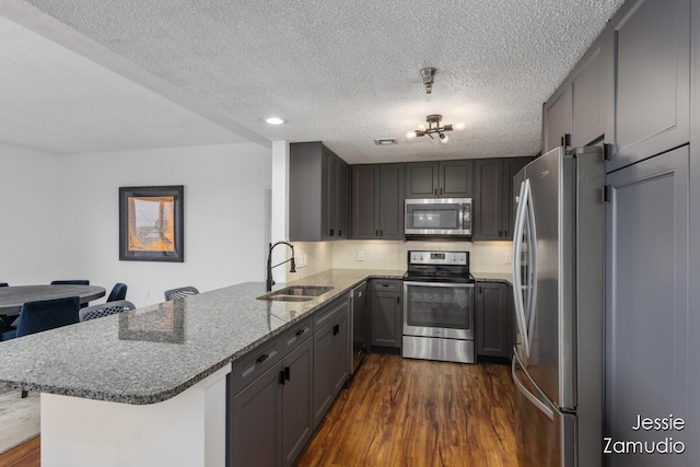 kitchen featuring stone counters, a peninsula, a sink, appliances with stainless steel finishes, and dark wood-style floors