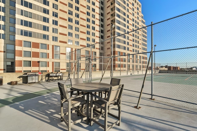 view of patio / terrace featuring a tennis court and fence