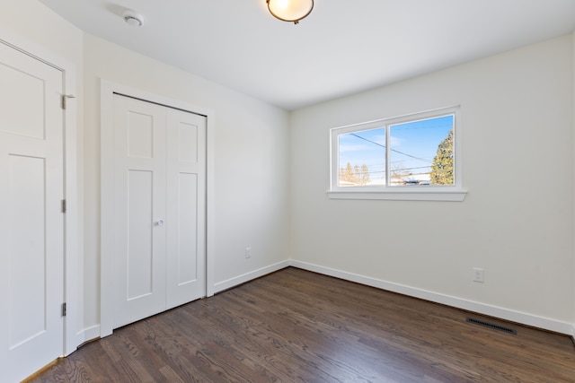 unfurnished bedroom featuring dark wood-style floors, a closet, visible vents, and baseboards