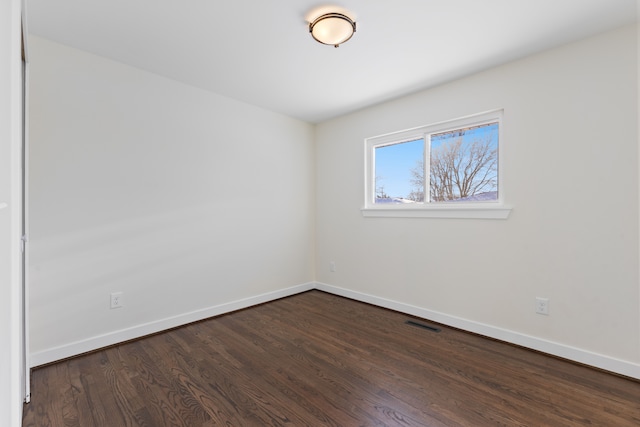 spare room featuring dark wood-style floors, visible vents, and baseboards