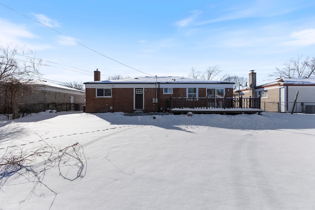 snow covered rear of property featuring a chimney, fence, and brick siding