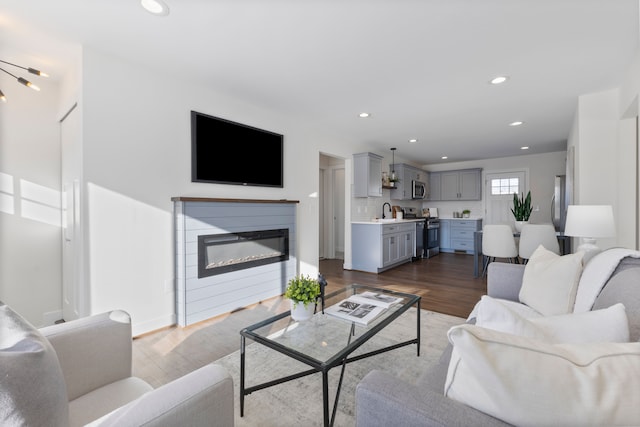 living room featuring dark wood-type flooring, a glass covered fireplace, baseboards, and recessed lighting