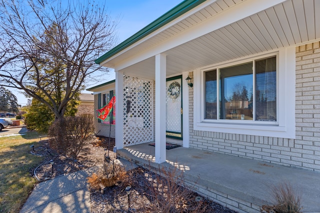 doorway to property featuring a porch and brick siding