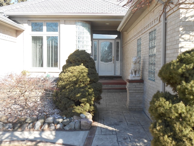 view of exterior entry featuring a high end roof and brick siding