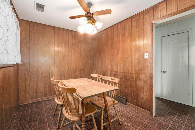 dining room with a ceiling fan, wood walls, visible vents, and baseboards