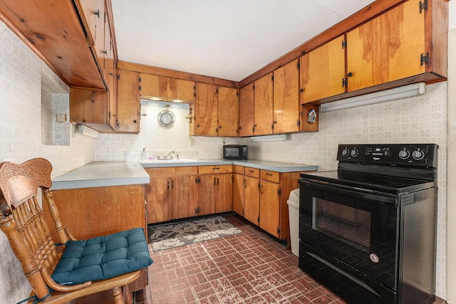 kitchen with brick floor, a sink, light countertops, black appliances, and brown cabinetry