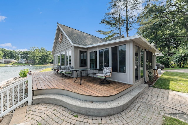 back of property featuring a sunroom, a deck with water view, and roof with shingles