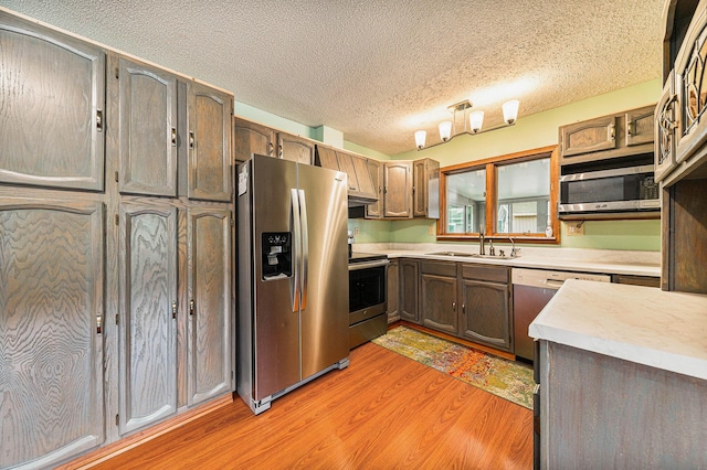 kitchen featuring light wood finished floors, stainless steel appliances, light countertops, a sink, and a textured ceiling