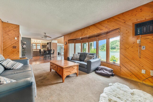 carpeted living room with a water view, wooden walls, a ceiling fan, and a textured ceiling