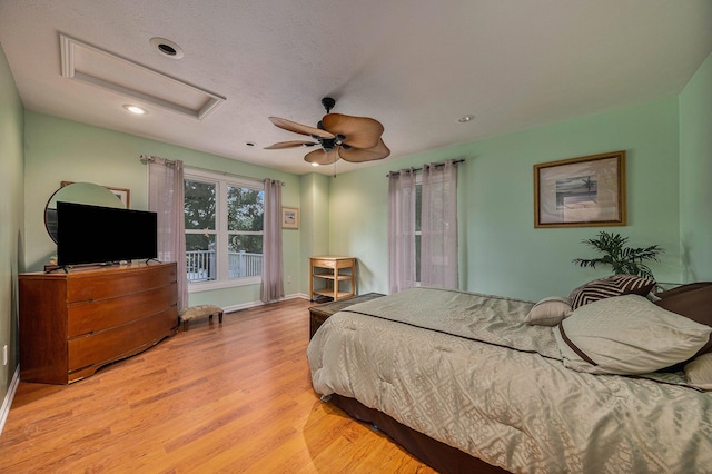 bedroom with attic access, baseboards, ceiling fan, wood finished floors, and a textured ceiling