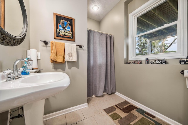 bathroom with curtained shower, a sink, a textured ceiling, baseboards, and tile patterned floors