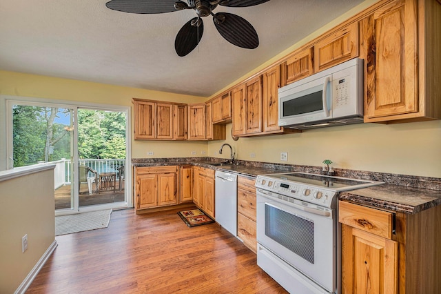 kitchen featuring brown cabinets, dark countertops, light wood-style flooring, a textured ceiling, and white appliances