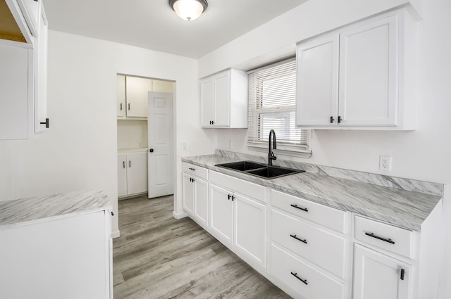 kitchen with light wood finished floors, a sink, light stone counters, and white cabinets