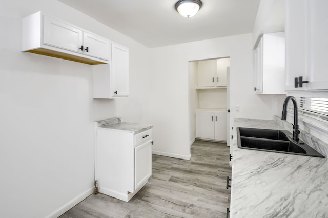 kitchen with baseboards, light countertops, light wood-type flooring, white cabinetry, and a sink