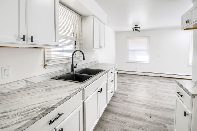 kitchen with light stone counters, baseboard heating, light wood-style floors, white cabinets, and a sink