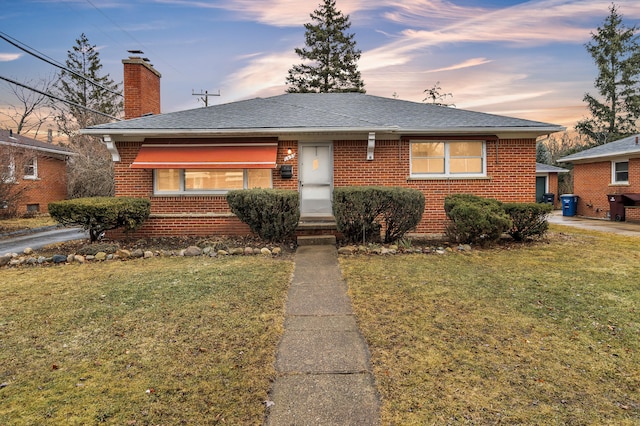 view of front of property with brick siding, a lawn, a chimney, and a shingled roof