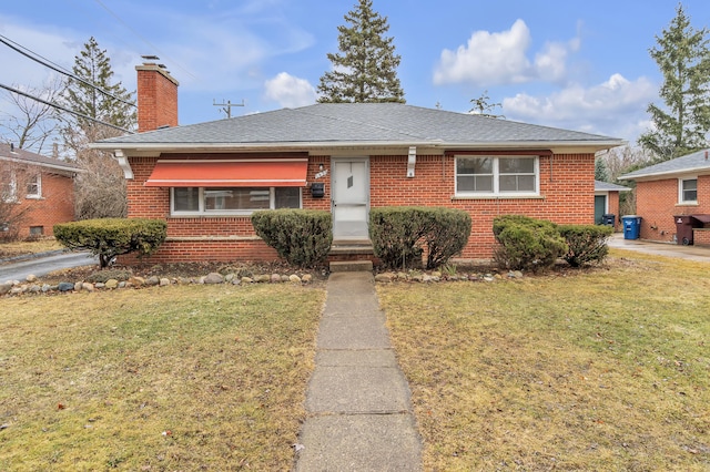 view of front of home featuring brick siding, a chimney, a front yard, and a shingled roof