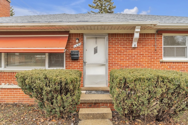 property entrance featuring brick siding and roof with shingles