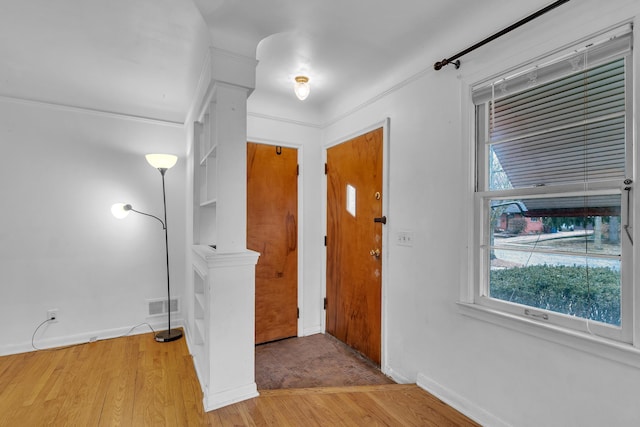 entrance foyer with ornamental molding, light wood-type flooring, visible vents, and baseboards