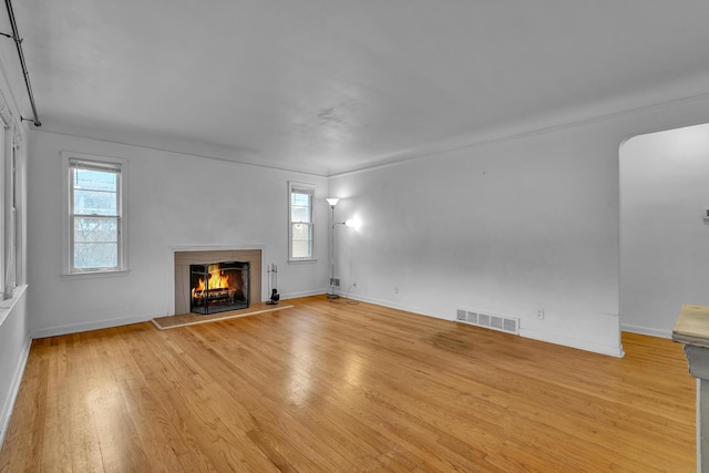 unfurnished living room with a warm lit fireplace, plenty of natural light, wood finished floors, and visible vents