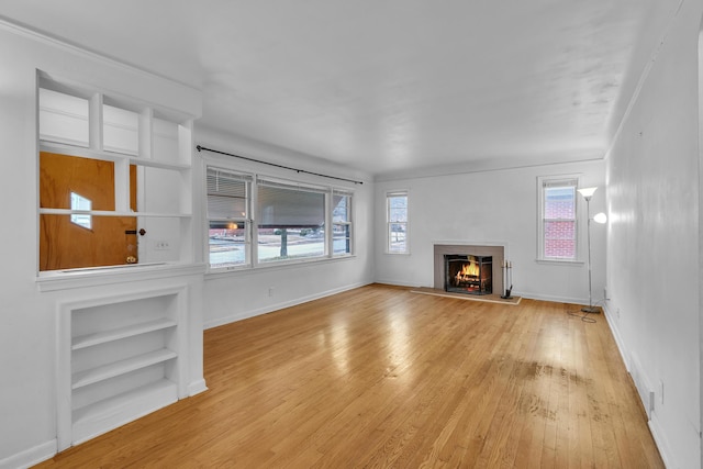 unfurnished living room featuring built in shelves, light wood-style floors, a lit fireplace, and baseboards