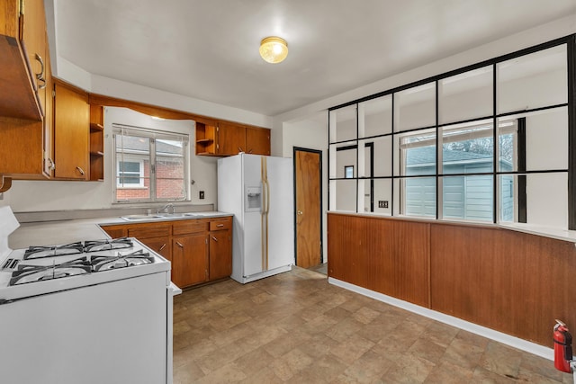 kitchen featuring white appliances, a sink, light countertops, open shelves, and brown cabinetry