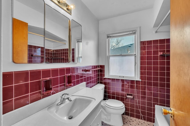 full bath featuring toilet, a wainscoted wall, vanity, tile walls, and a tub