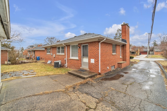 exterior space featuring aphalt driveway, brick siding, a chimney, entry steps, and cooling unit