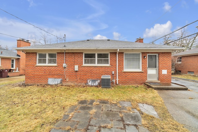 back of property with brick siding, a chimney, central AC unit, and a lawn