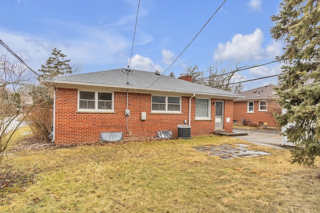 back of property with cooling unit, brick siding, a shingled roof, a yard, and a chimney