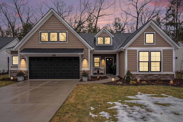 craftsman-style house featuring a shingled roof, a lawn, concrete driveway, stone siding, and an attached garage