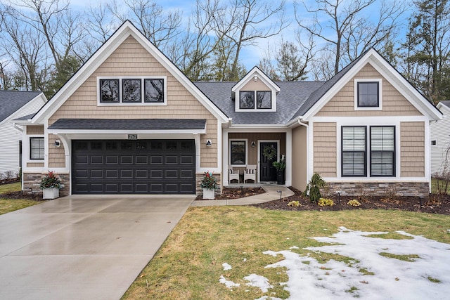 craftsman-style house with a shingled roof, concrete driveway, an attached garage, stone siding, and a front lawn