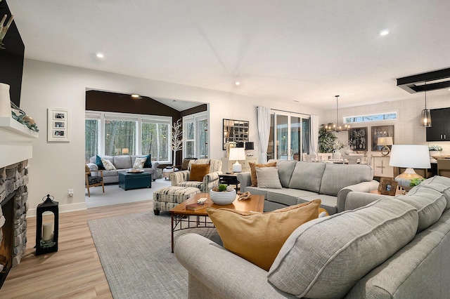 living room with a chandelier, a stone fireplace, recessed lighting, baseboards, and light wood-style floors