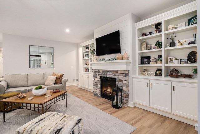 living room featuring built in shelves, a stone fireplace, visible vents, baseboards, and light wood-type flooring