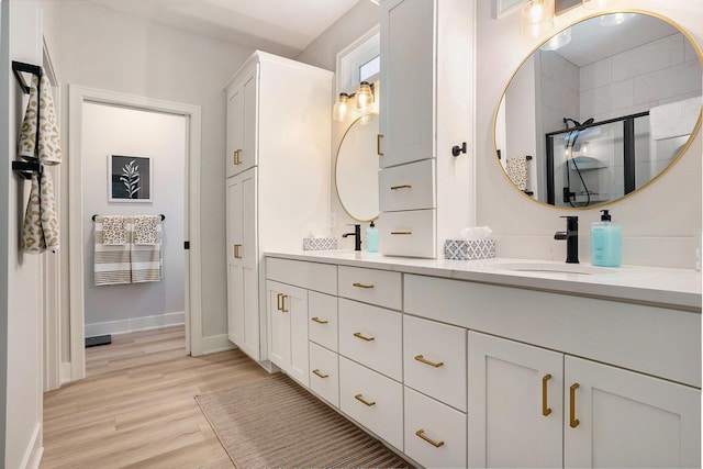 bathroom featuring a sink, wood finished floors, baseboards, double vanity, and a stall shower