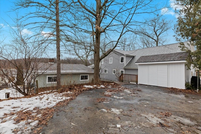 view of property exterior with an outbuilding, driveway, roof with shingles, and an attached garage