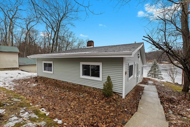 view of side of home with roof with shingles and a chimney