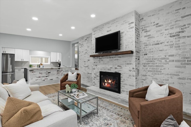 living area with a brick fireplace, light wood-style flooring, and recessed lighting