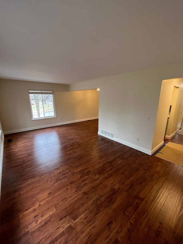 empty room featuring baseboards, visible vents, and dark wood-style flooring